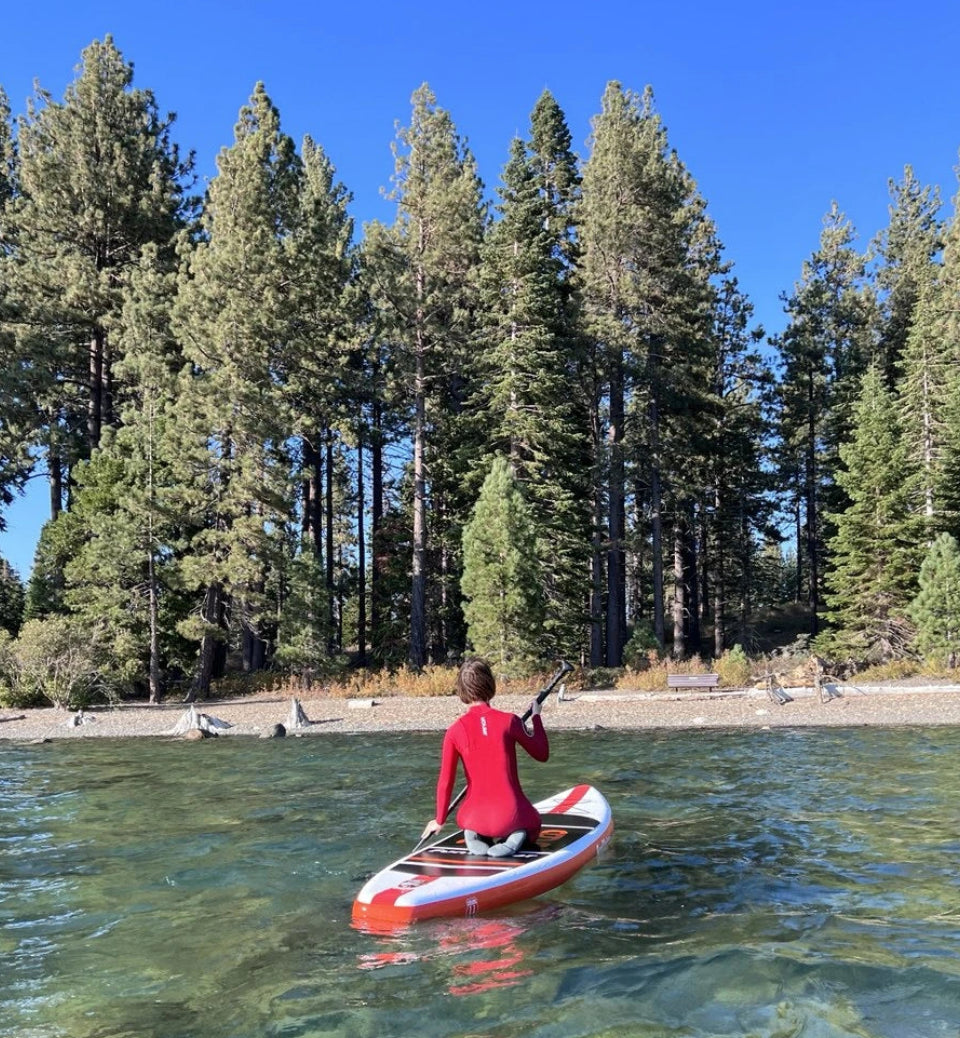 Person in a red wetsuit paddleboarding on a lake with trees in the background