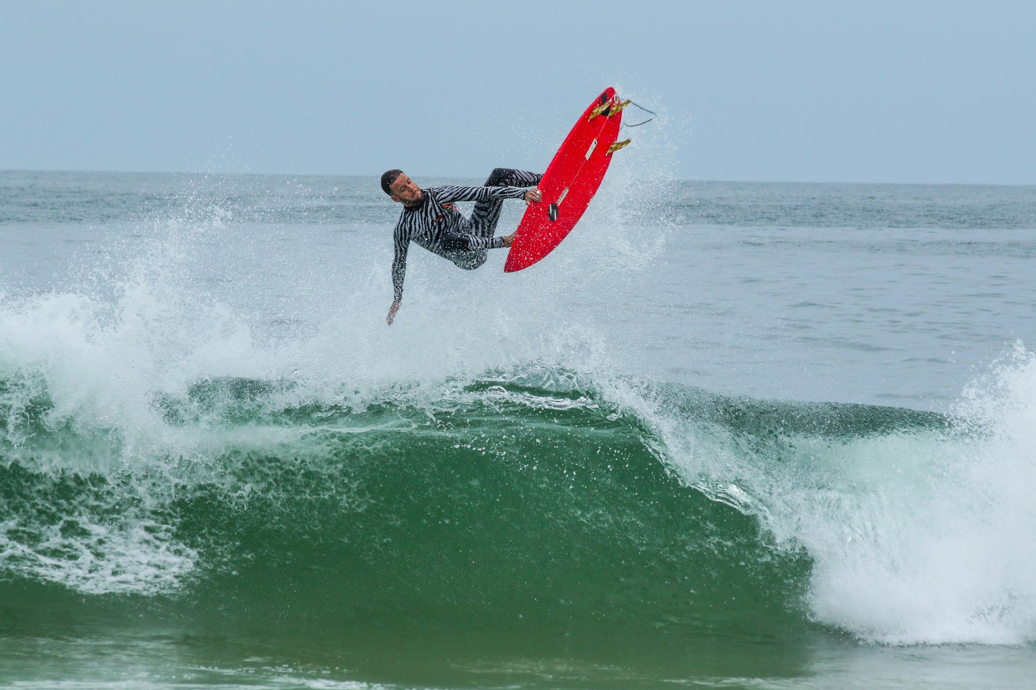 Surfer in JANGA ZEBRA wetsuit on a red surfboard performing a trick in the ocean.