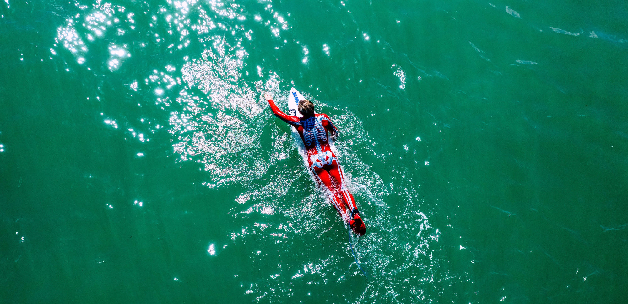 surfer paddling in a deep green ocean wearing red JANGA wetsuit