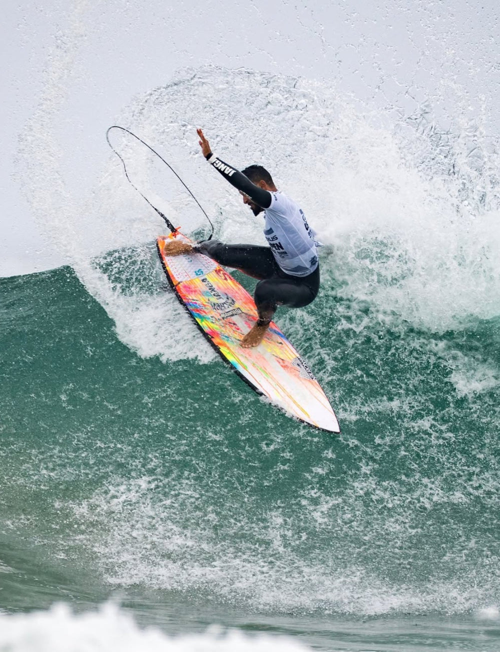 Surfer michaelrodrigues85 riding a wave on a colorful surfboard in a JANGA wetsuit